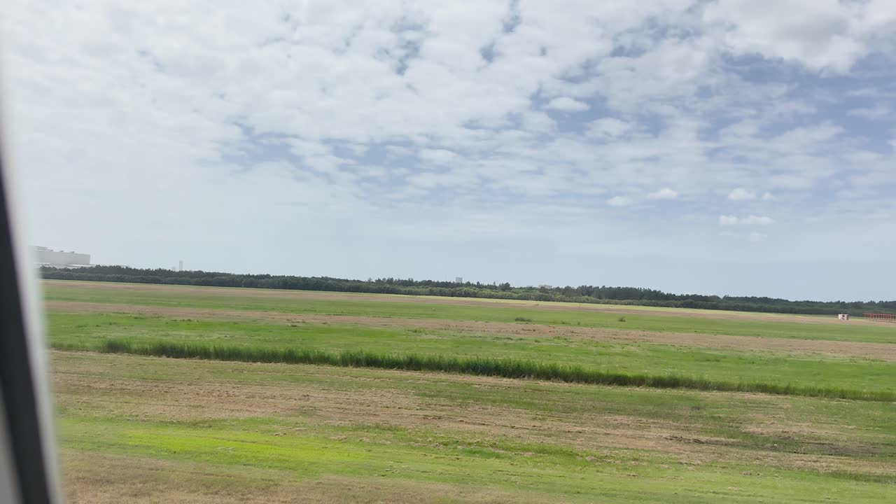 Fly bevæger sig langs landingsbane, klart dagslys, bredt udsyn over marker gennem flyvinduet, roligt kamera