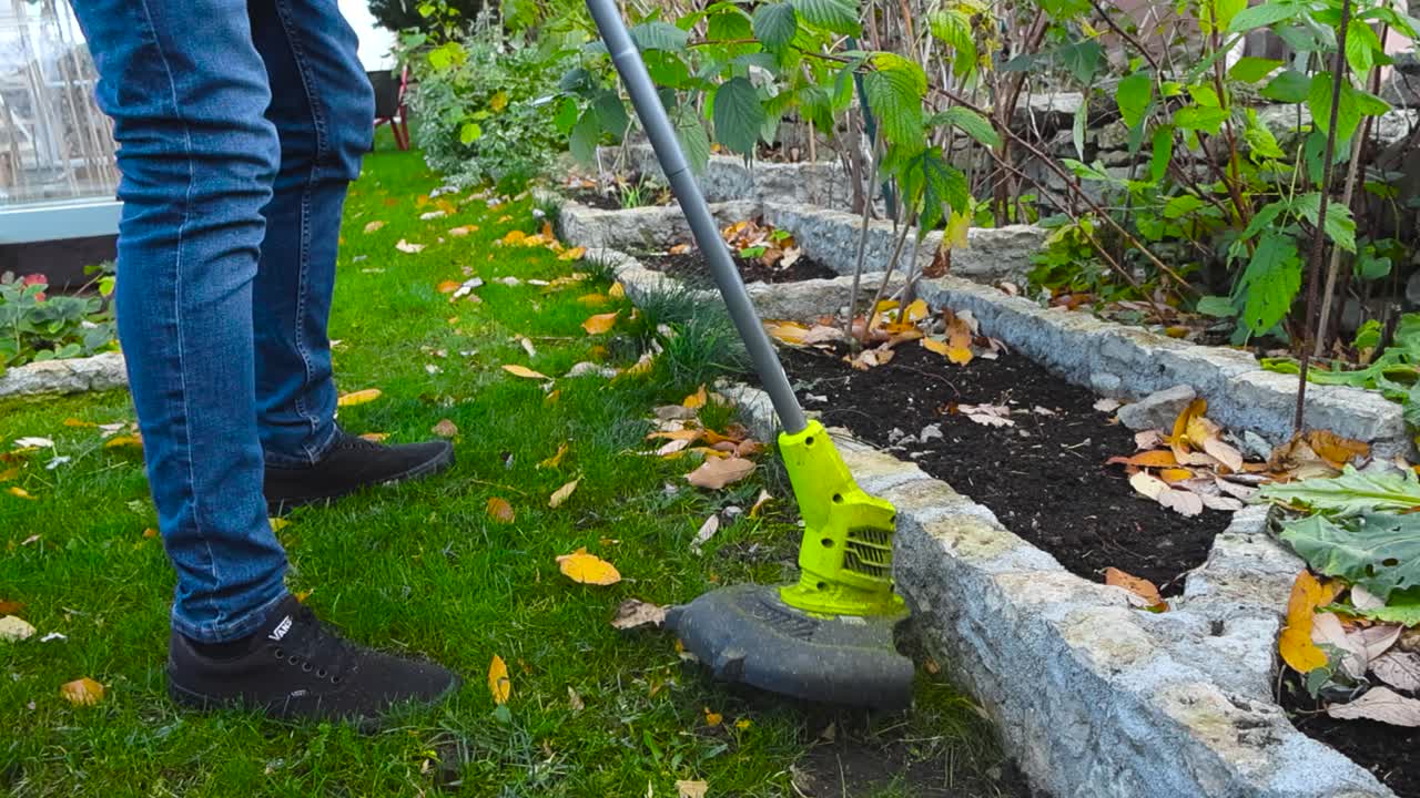 Man using a weed wacker to trim grass and weeds in a garden