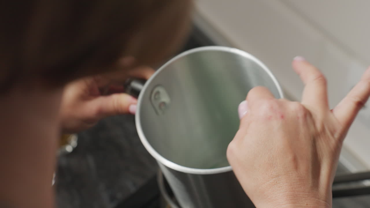 Rear view of woman stirring contents inside metal container during craft preparation process, focusing intently on mixing ingredients carefully in kitchen environment