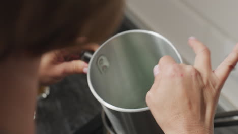 rear view of woman stirring contents inside metal container during craft preparation process, focusing intently on mixing ingredients carefully in kitchen environment