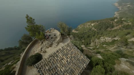 fpv drone tiro giratorio sobre el mirador de ricardo roca a lo largo de un acantilado que domina el mar azul profundo en illes balears, españa durante el día