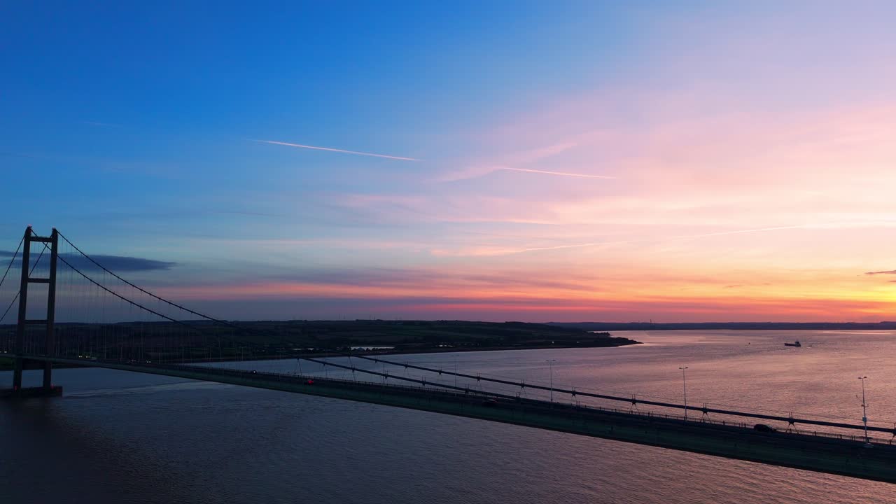 An aerial drone's lens unveils the Humber Bridge aglow in a serene sunset, with cars elegantly crossing