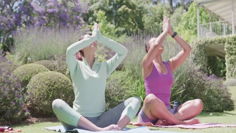 Happy-biracial-sisters-doing-yoga-and-meditating-in-garden,-in-slow-motion