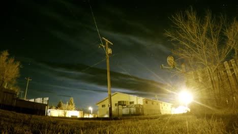 Noche---Nubes-Y-Estrellas-En-El-Cielo-Nocturno-Sobre-Un-Edificio-Con-Luces-De-La-Calle-Y-Arbustos-Alrededor