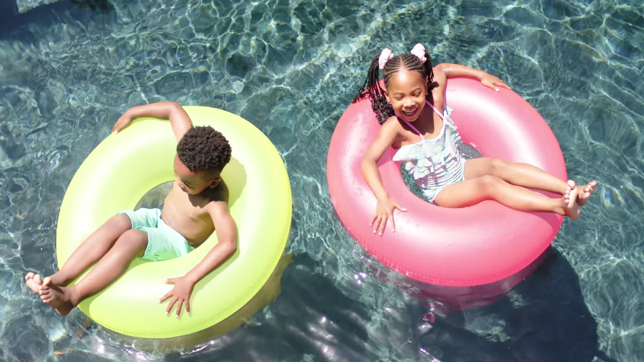 hermanos africanos americanos felices con inflables en la piscina, en cámara lenta