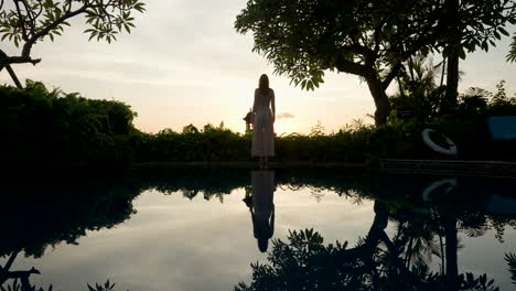 female silhouette alone, darkness covers vegetation, water reflections