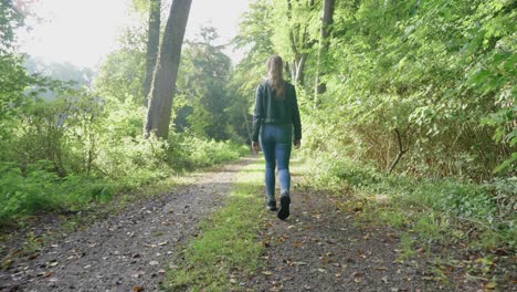 young female strolls along road in woods on bright day, tracking