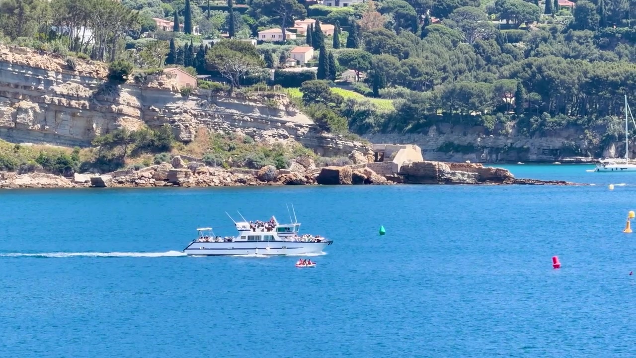 Una barca passeggeri bianca naviga attraverso le acque blu del Mediterraneo oltre scogliere frastagliate in Provenza.
