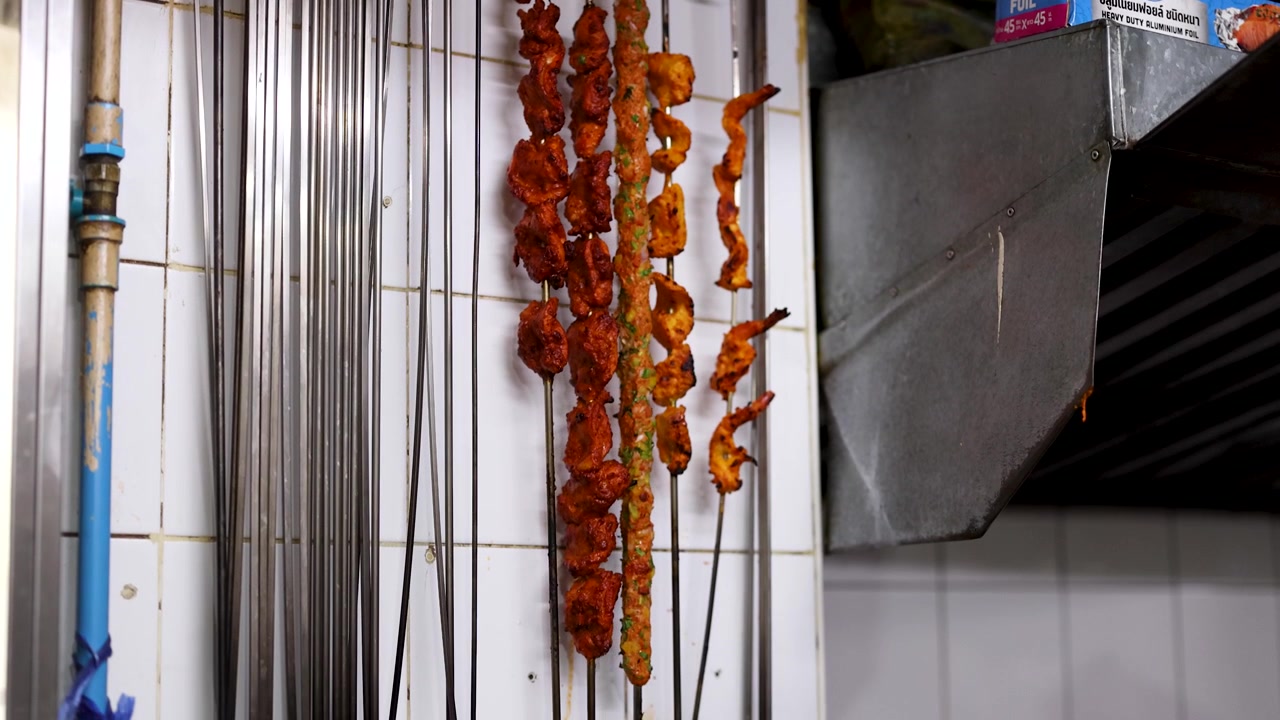 Inquadratura media statica di spiedini di carne speziati appesi in una cucina commerciale prima della cottura alla griglia