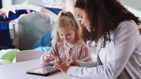 maestra de escuela infantil trabajando uno a uno con una joven escolar blanca usando una tableta, de cerca