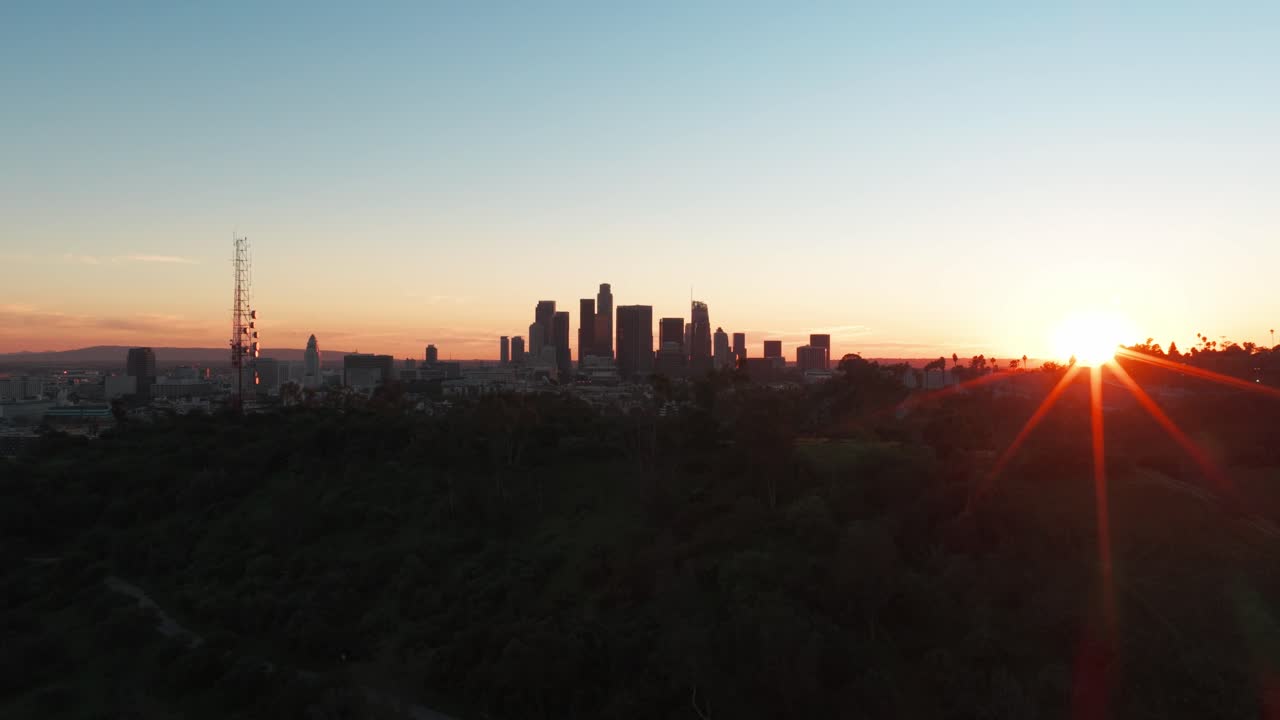 Toma aérea con paneo bajo del centro de Los Ángeles con destello de sol durante el atardecer en el sur de California. En 4K.