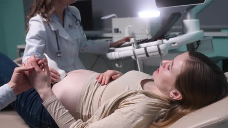 pregnant woman having ultrasound scan at the gynecologist office while loving husband holding her hand 11