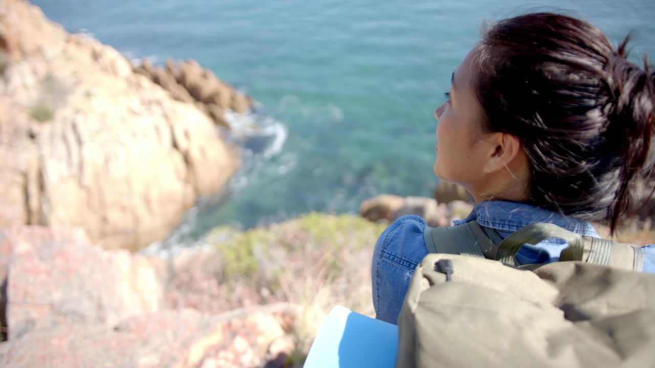 Hiking with backpack, woman enjoying scenic ocean view from mountain cliff