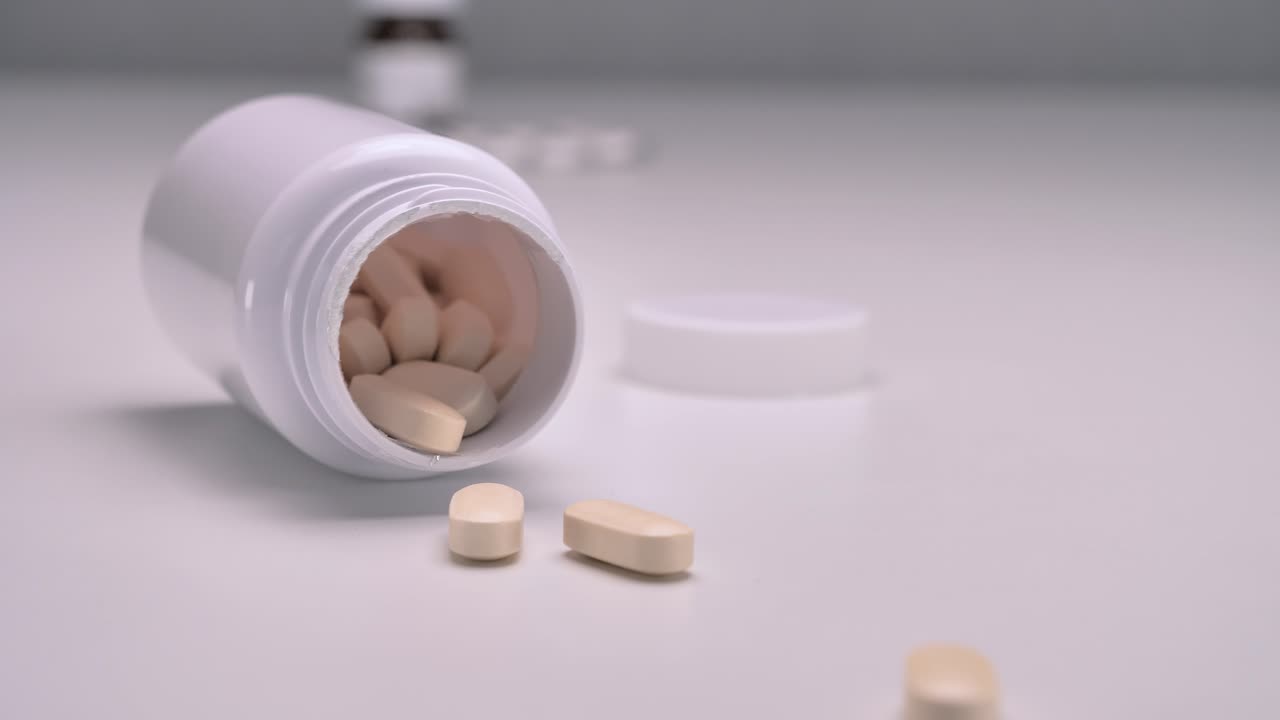 백색 의약품 병이 테이블에 떨어지고 약이 흘러나옵니다.