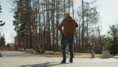 a father playfully spins his son around in an outdoor park, lifting him up and down with joy, with trees in the background