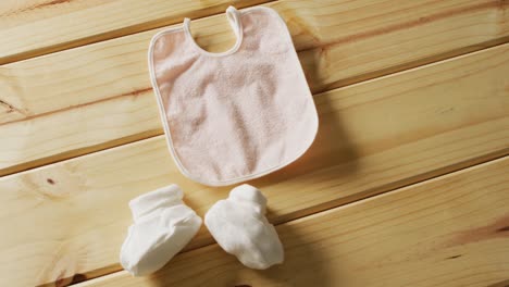 Video-of-close-up-of-pink-baby-bib-with-white-booties-on-wooden-background
