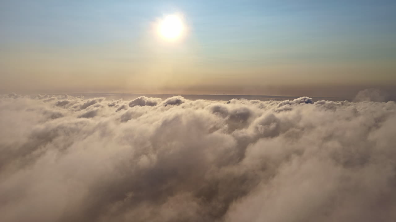 Fling high above a vast and peaceful sea of fluffy clouds, moving towards the bright sun shining in the hazy sky, creating a majestic and heavenly scene at sunset in Latvia