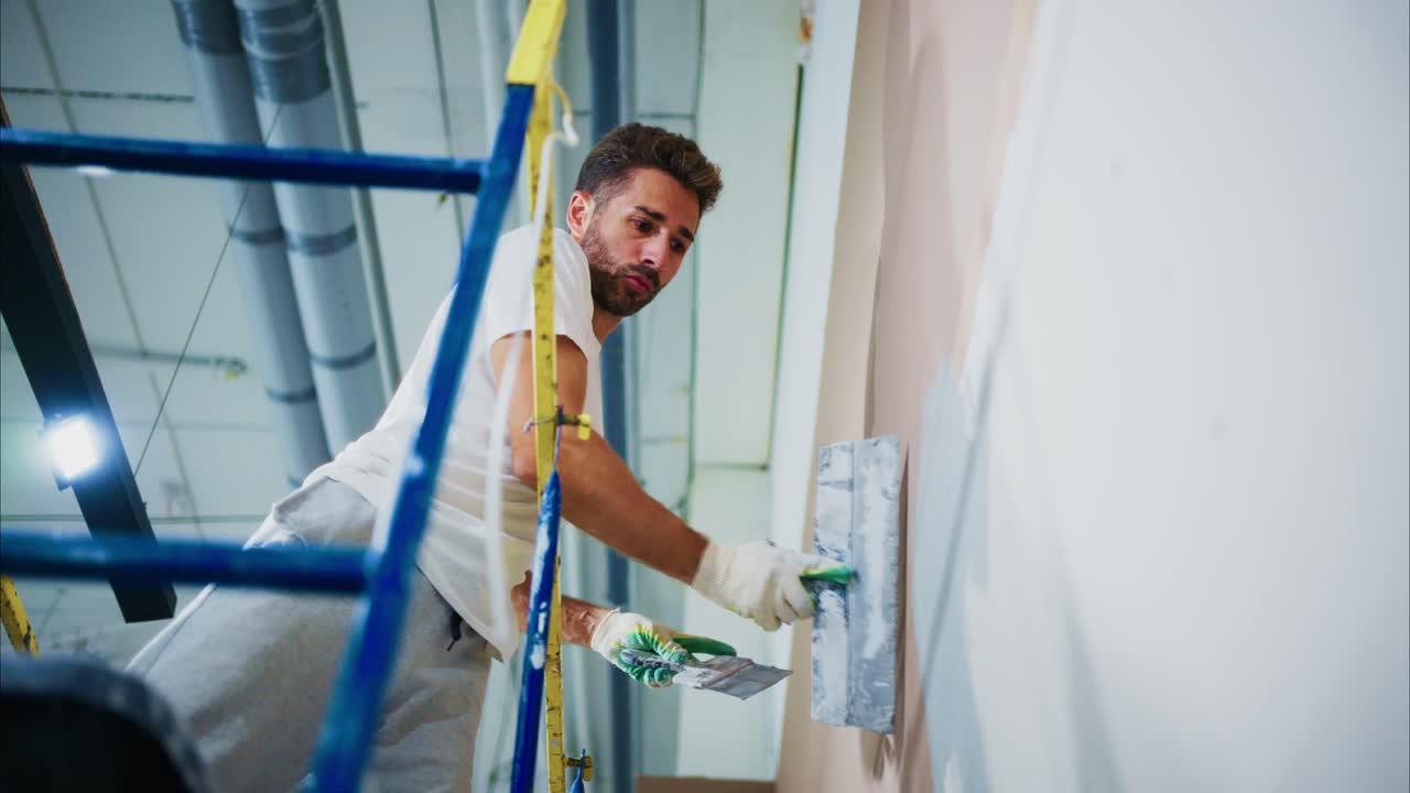 A Skilled Worker Using Tools on a Scaffold to Smooth and Prepare a Wall for Painting or Finishing in a Brightly Lit Interior Space