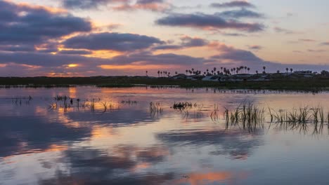 Beautiful-golden-sunset-timelapse-with-light-rays,-flowing-clouds-and-water-slowly-flowing-at-reflective-mirror-lake