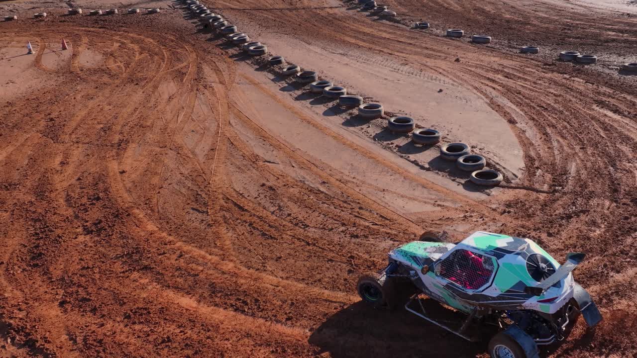 Buggy terenowe driftuje po czerwonej ziemi z barierami z opon. – ujęcie z lotu ptaka