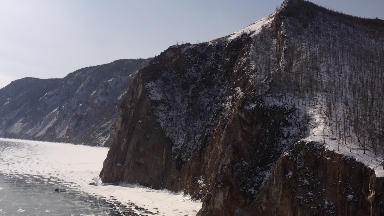 un vuelo circular desde el lago congelado baikal hasta la orilla rocosa cubierta de bosque.