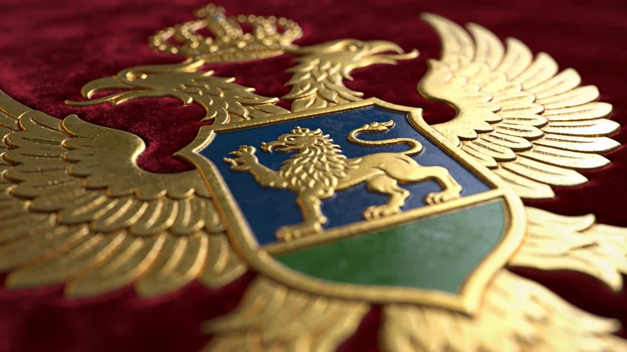 Kamera na pojezdu skenuje dvouhlavého orla na červeném sametu, ukazující pozlacené detaily a motiv lva na štítu.