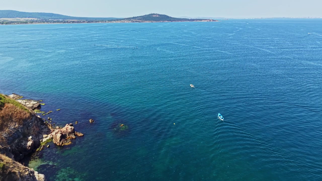 Vista di un mare calmo e barche vicino a una costa rocciosa durante il giorno, vicino a una città in una regione costiera.