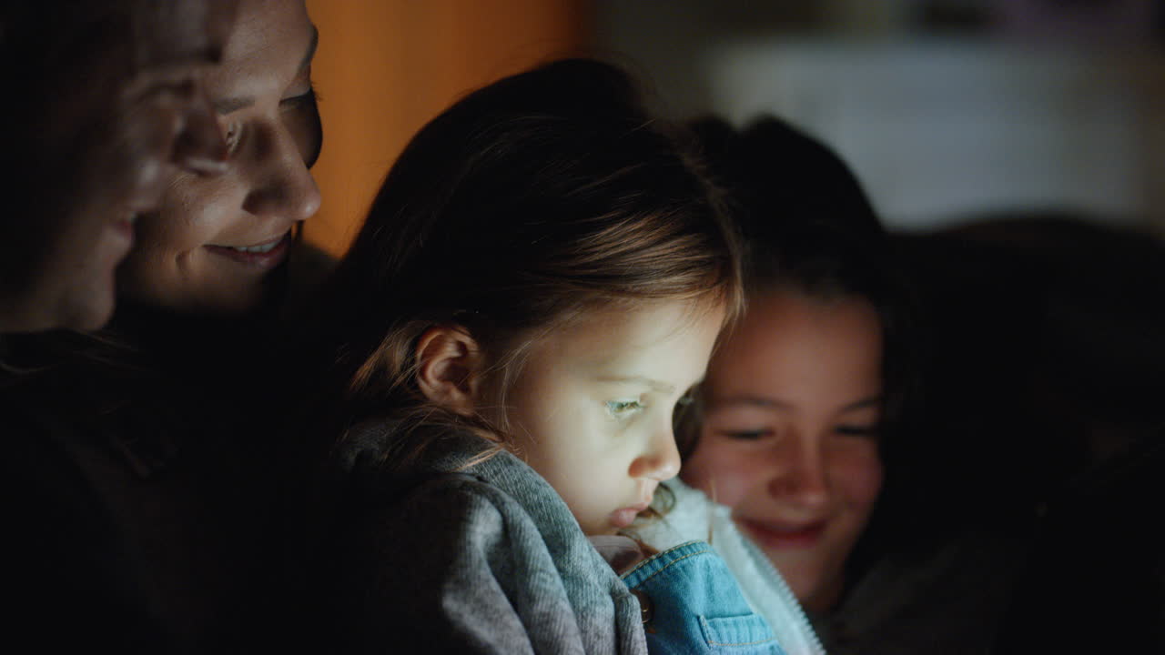 태블릿 컴퓨터를 사용하는 가족 어린 소녀는 터치 스크린 기술을 통해 어머니와 아버지와 함께 엔터테인먼트를보고 잠자리에 들기 전에 휴식을 즐기고 있습니다. 4k