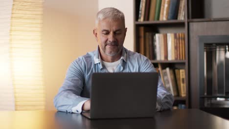 hombre mayor trabajando en una computadora portátil en casa