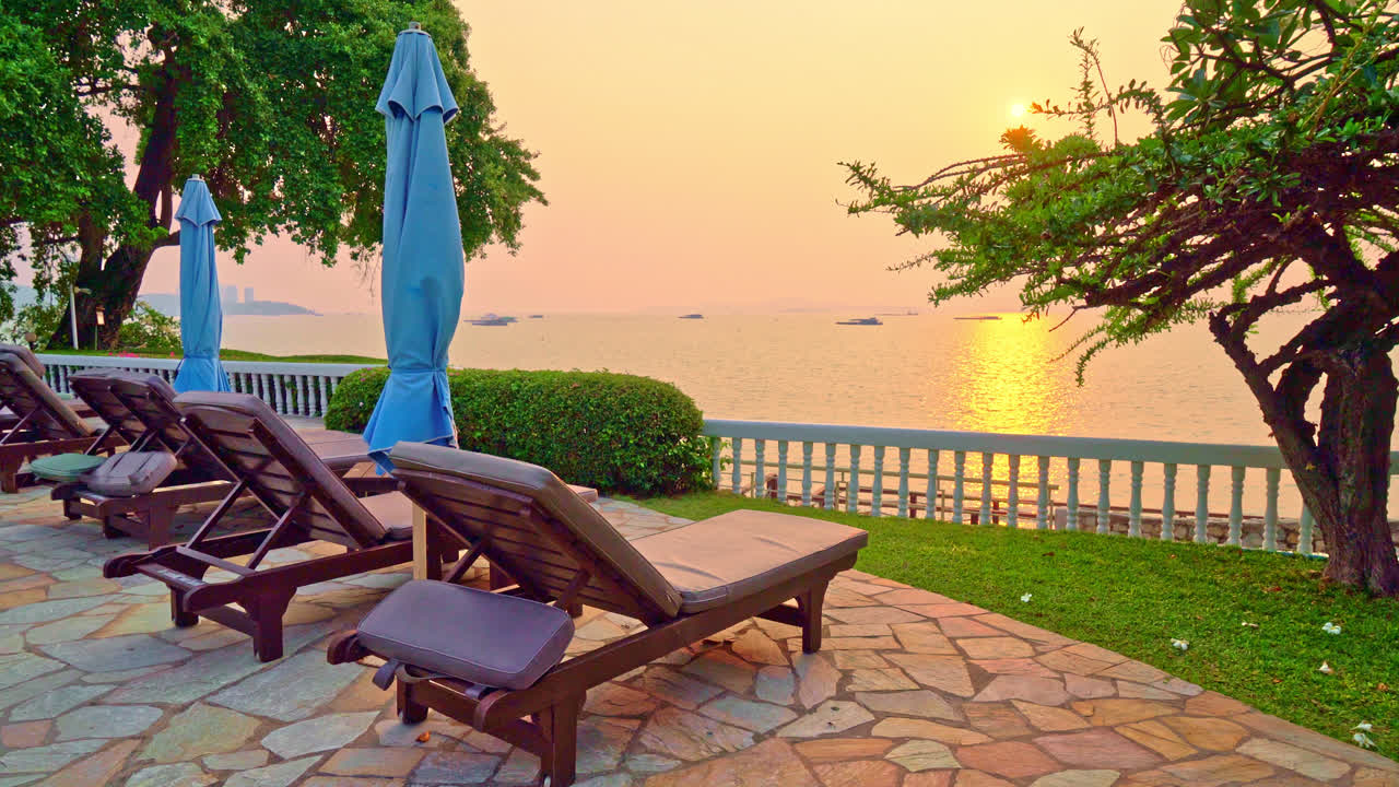 일몰 시간에 수영장 주변에 우산이있는 해변 의자 또는 수영장 침대