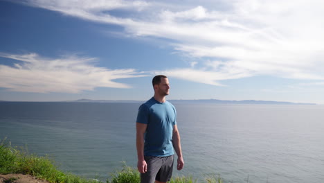 Un-Hombre-Fuerte-En-Forma-De-Pie-Orgulloso-Al-Borde-De-Una-Ruta-De-Senderismo-Por-La-Naturaleza-Del-Acantilado-Del-Océano-Con-Una-Vista-épica-De-La-Playa-En-Un-Día-Soleado-En-Cámara-Lenta-De-Santa-Bárbara,-California