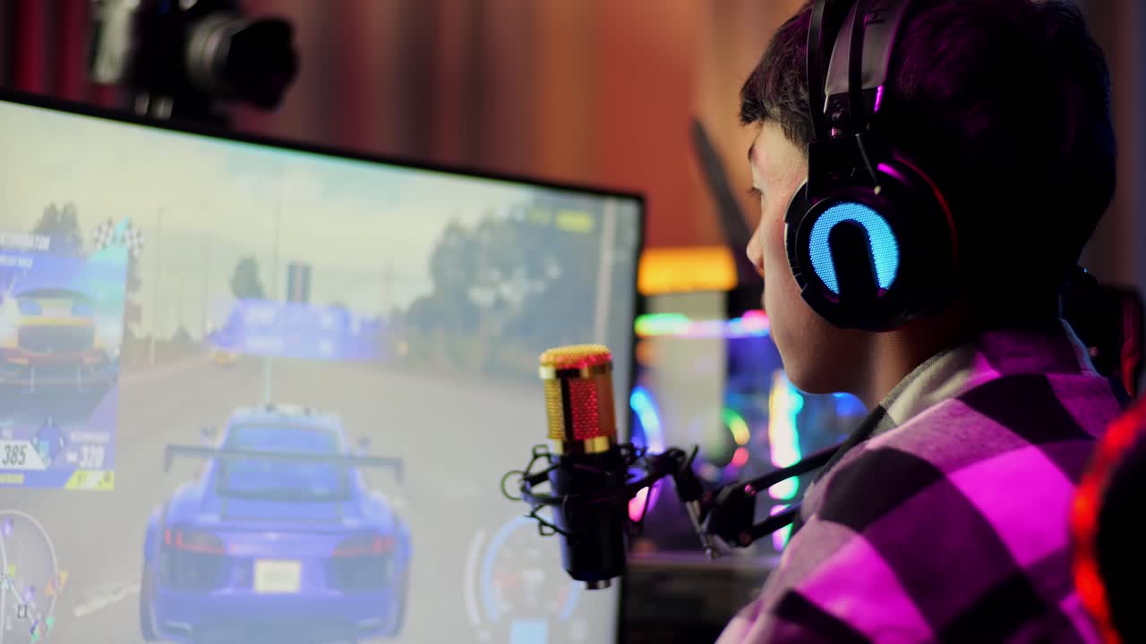 아시안 소년 스트리머가 컴퓨터에서 네트워크를 통해 자동차 레이싱 게임을하고 마이크를 통해 이야기하고 있습니다. 라이브 스트리밍 비디오 게임, rgb led 스트립 라이트에 의해 조명 된 책상