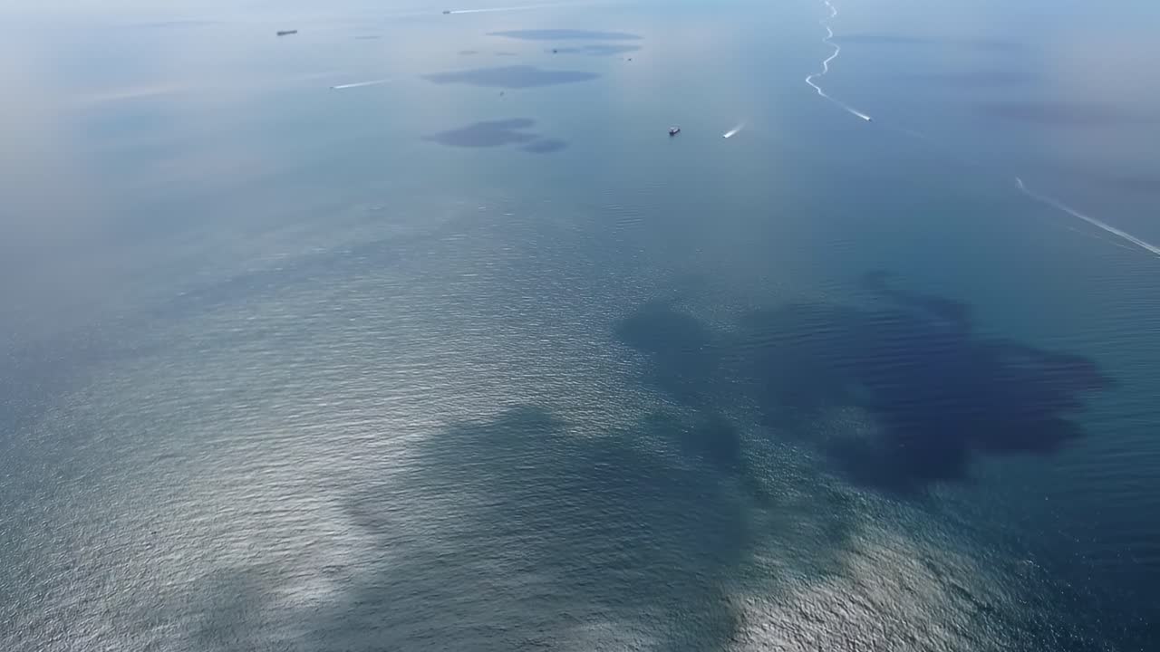 Aerial View of Tranquil Ocean Waters with Distant Ships and Reflection Patterns on the Surface, Capturing the Serenity of Maritime Life