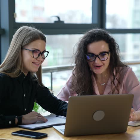 two women colleagues discuss something in computer in office. female teammates wearing glasses work in front of laptop