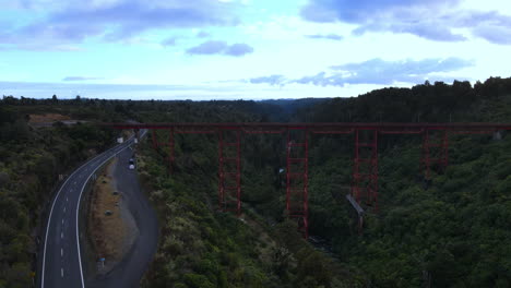 Drone-Pullback-Shot-Der-Roten-Eisenbahnbrücke-über-George-Mit-Bäumen-Und-Fluss-Und-Straße