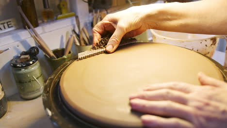 close up of male potter shaping clay for house sign on pottery turntable in ceramics studio