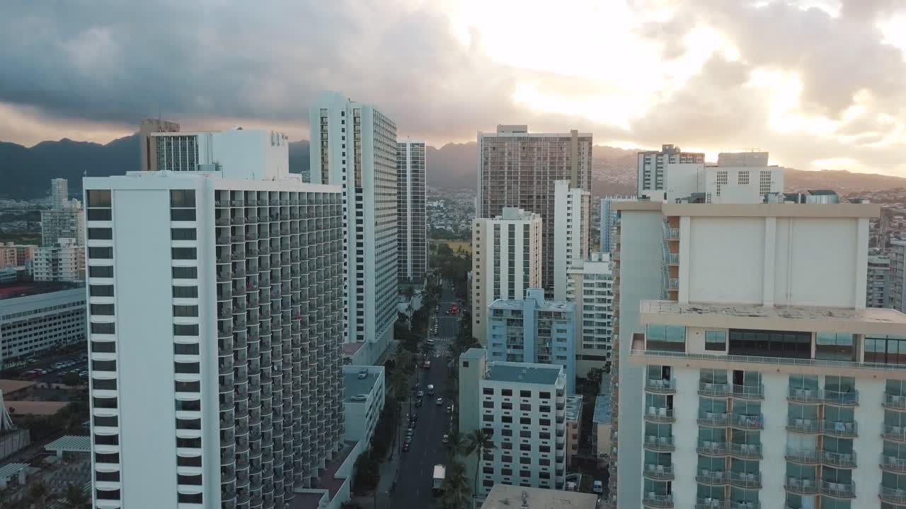 Panning aerial drone slowly flying over a colorful Honolulu Skyline while Sunset in Oahu, Hawaii with Waikiki Beach as a special point of interest.