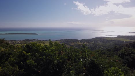 una toma panorámica que se mueve a la derecha de la isla mauricio, que muestra el paisaje lleno de vegetación, el océano, una pequeña isla y un cielo despejado y sorprendente