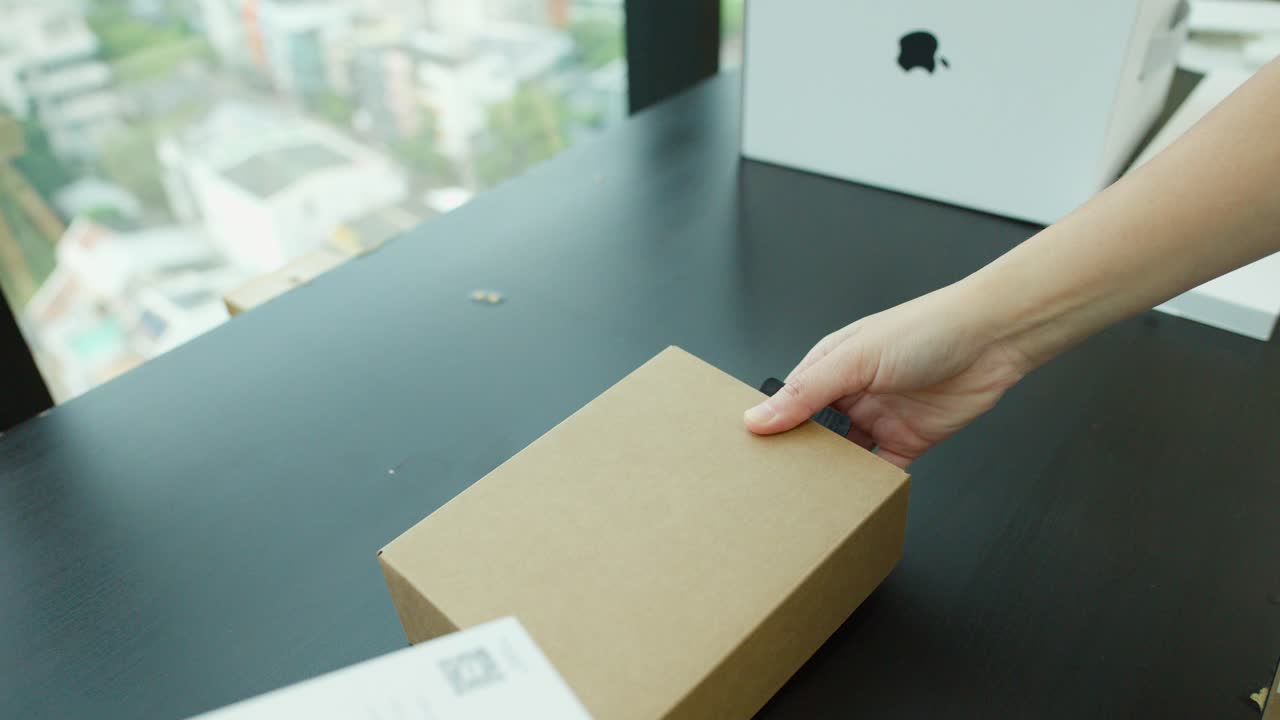 Hands unbox a computer mouse on a black desk with natural daylight and steady camera