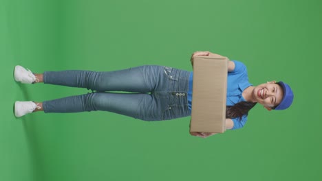 full body of asian female courier in blue uniform showing a carton to camera and smiling while delivering it on green screen background in the studio