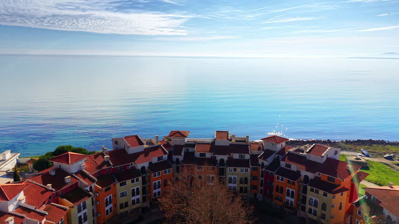 Edificio semicircolare a più piani con tetti in terracotta situato vicino a un faro e alla riva del mare. Veduta aerea di un condominio.
