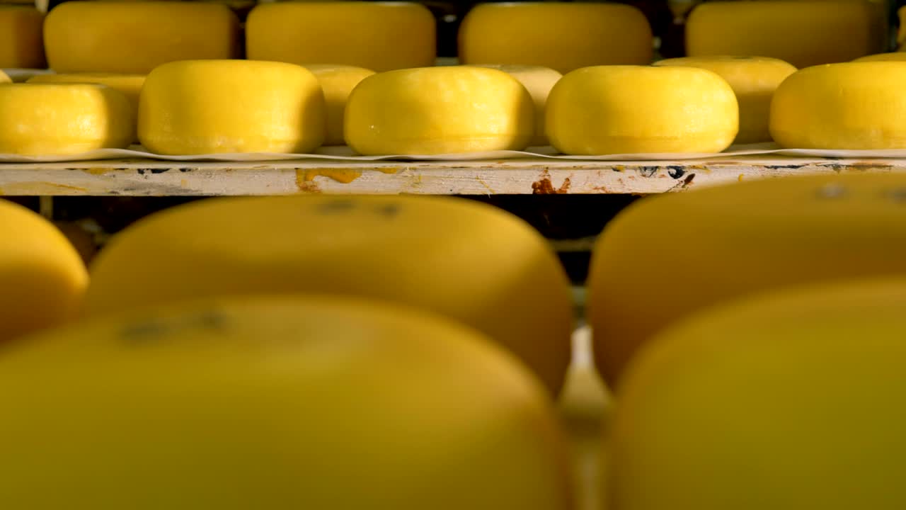 ruedas de queso en un estante de almacenamiento con otra fila borrosa más cerca.