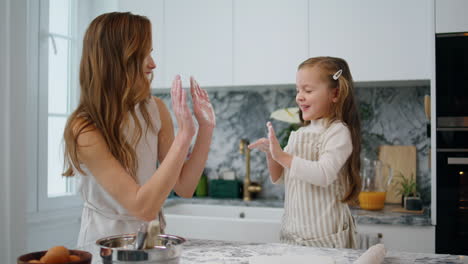 madre alegre niño aplaudiendo en la cocina. mujer juguetona y niña divirtiéndose