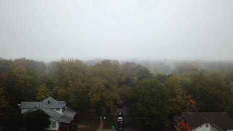 aerial shot above a residential block with autumnal trees with heavy fog