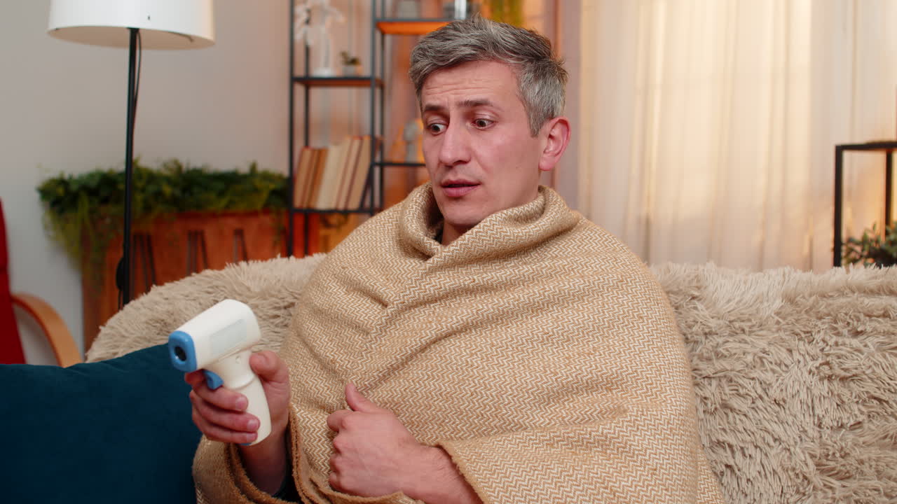 Young man checks body temperature with thermometer looks worried about possible illness and fever