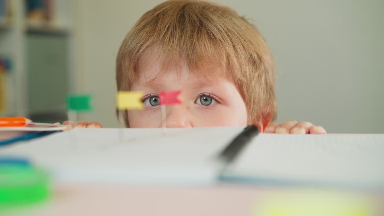 el niño mira los alfileres con banderas en el cuaderno escondido detrás de la mesa