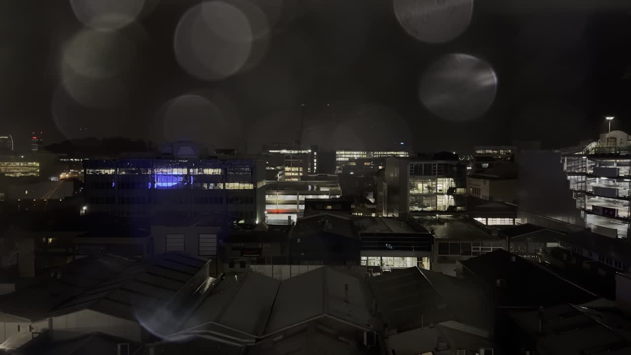 wide shot of city evening buildings and lights with some raindrop falling from the window