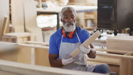 african american male carpenter looking and choosing wooden plank in a carpentry shop