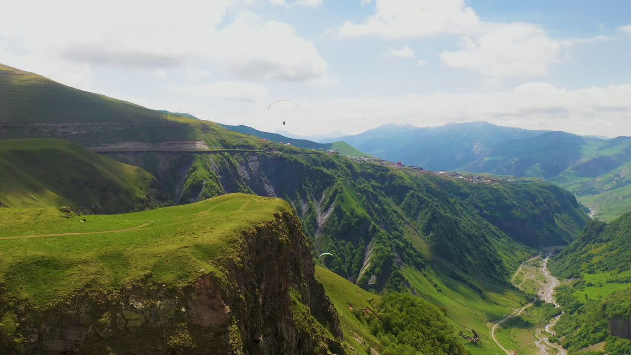 amplia toma de drones de las montañas del cáucaso con gente haciendo parapente en la distancia en gudauri georgia
