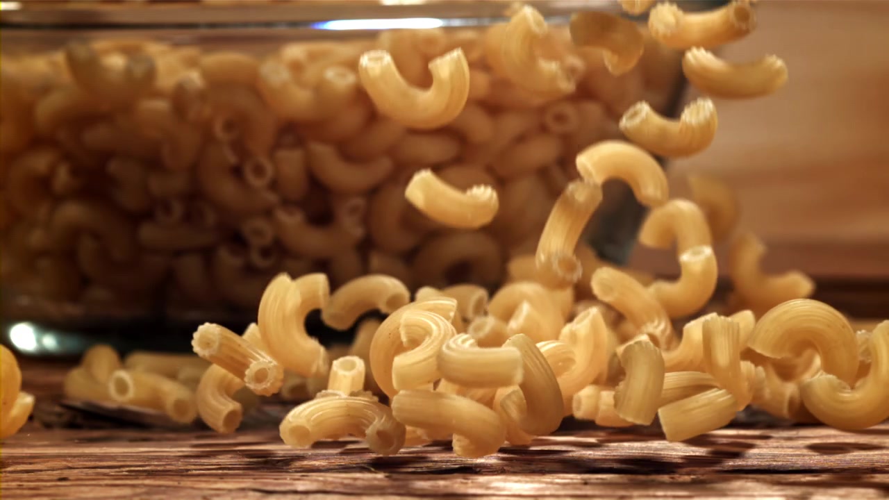 Maccheroni a gomito che cadono al rallentatore su una superficie di legno